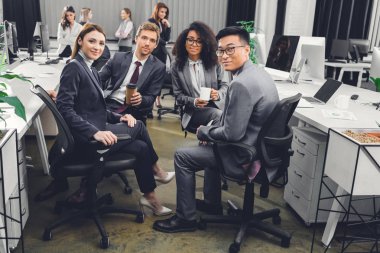 birlikte oturan ve kamera Office gülümseyen genç çok ırklı iş adamları resmi giyim   