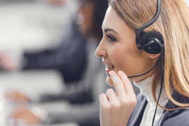 Genç kadın teleworker gülümseyerek ve çalışma office kulaklık yan görünüm