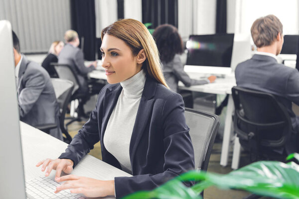beautiful smiling young businesswoman using desktop computer while working with colleagues in open space office