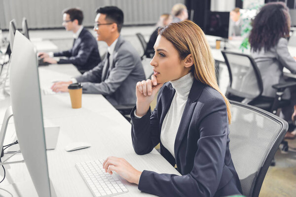concentrated young businesswoman using desktop computer while working with colleagues in open space office