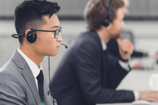 side view of focused young asian businessman in headset working with colleagues in office