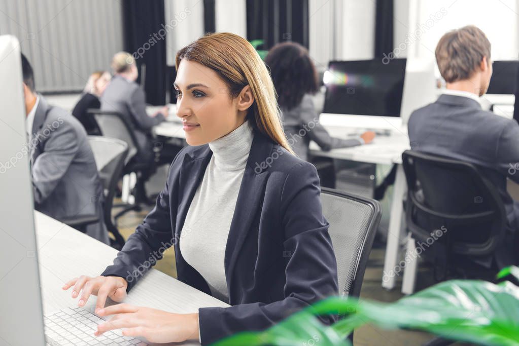 beautiful smiling young businesswoman using desktop computer while working with colleagues in open space office