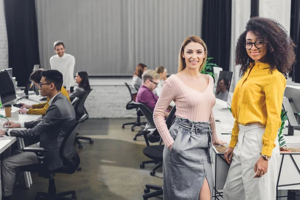 Jóvenes Empresarias Multiétnicas Sonriendo Cámara Mientras Sus Colegas Trabajan Detrás — Foto de Stock