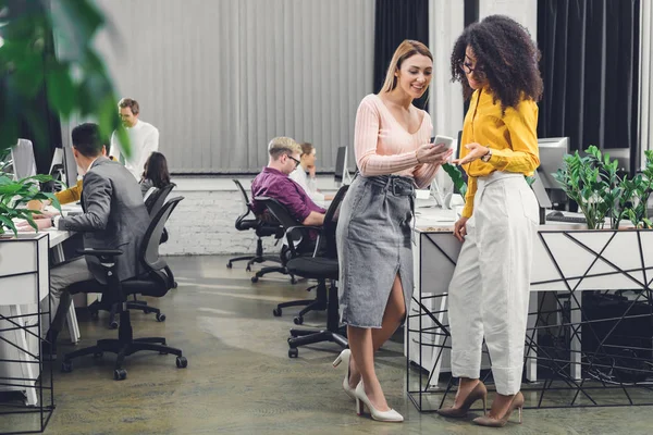 Giovani Imprenditrici Sorridenti Che Utilizzano Smartphone Parlano Mentre Colleghi Lavorano — Foto Stock