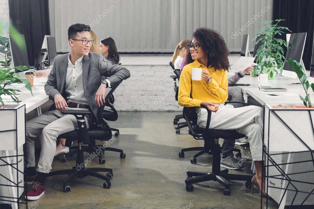 Happy young multiethnic businesspeople smiling each other while working together in office
