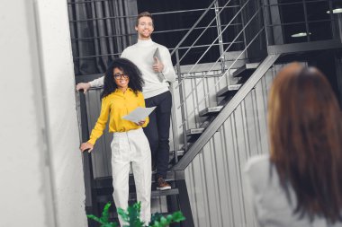 merdiven üzerinde duran ve modern ofiste gülümseyen çok ırklı genç iş adamları