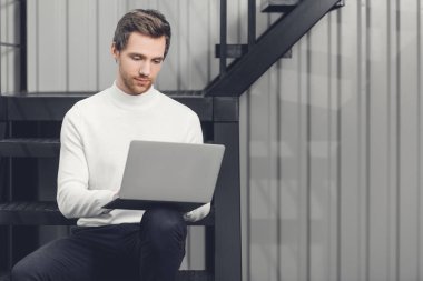 merdivenlerde oturan ve dizüstü bilgisayar kullanma office gülümseyen yakışıklı genç