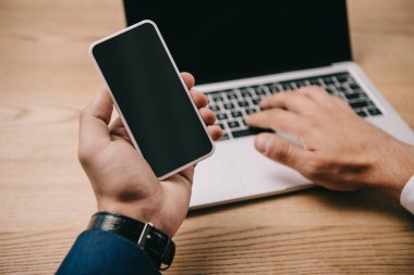 smartphone işyerinde laptop yazarken tutan işadamı kırpılmış görünümü