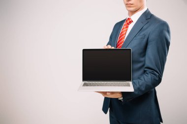 cropped view of businessman in suit showing laptop isolated on grey clipart