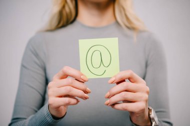 Kırpılan görünümü gri izole e-posta işareti ile kağıt not tutan kadın