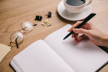 Kadın defter gözlük ve kahve ile işyerinde yazma kısmi görünümünü