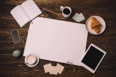 ahşap masa üzerinde boş kağıt, iş malzemeleri, kruvasan ve kahve Kupası üstten görünüm