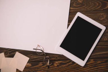 ahşap masa üzerinde dijital tablet, gözlük ve boş kağıt üstten görünüm