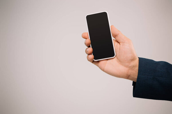 cropped view of businessman holding smartphone with blank screen isolated on grey