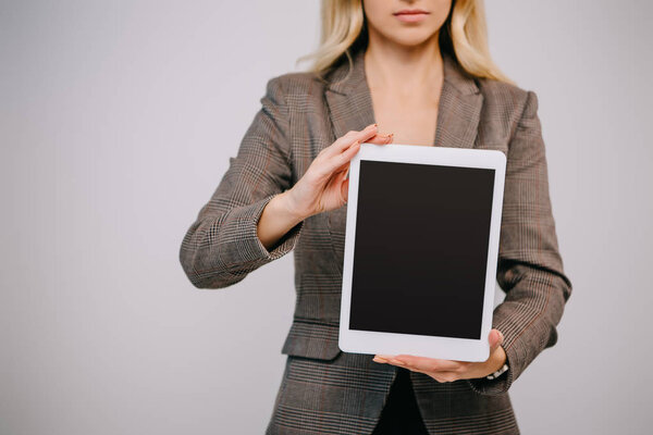 cropped view on businesswoman in suit presenting digital tablet with blank screen isolated on grey