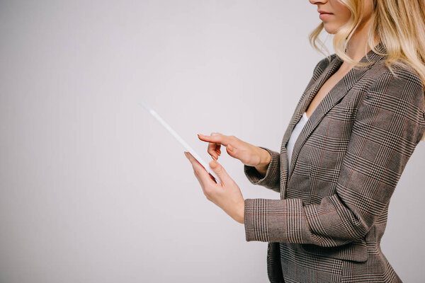 cropped view on businesswoman in suit touching digital tablet isolated on grey