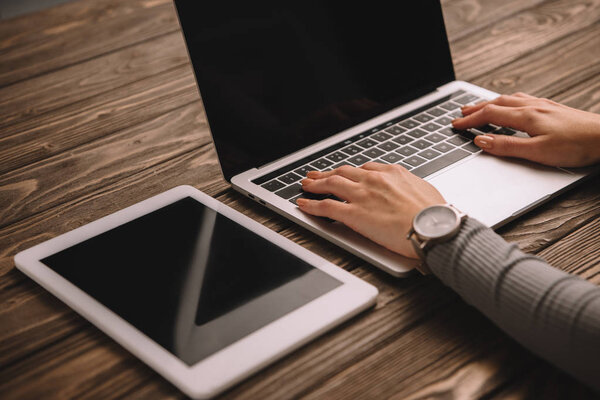 cropped view of businesswoman typing on laptop at workplace with digital tablet