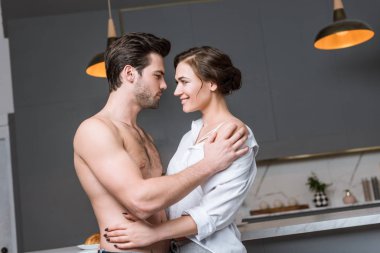 adult couple embracing and smiling at kitchen and looking into eyes clipart