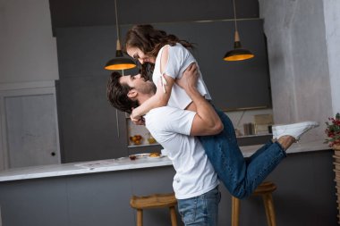 handsome man holding in arms attractive girlfriend in modern kitchen  clipart
