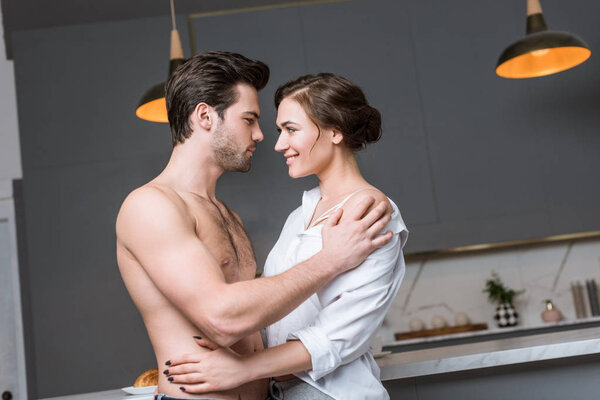 adult couple embracing and smiling at kitchen and looking into eyes
