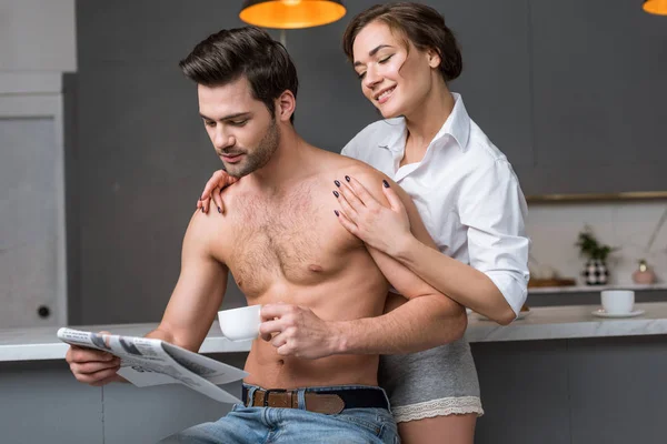 Mulher Sorrindo Abraçando Homem Sem Camisa Lendo Jornal Enquanto Segurando — Fotografia de Stock