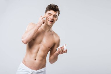 mutlu gömleksiz adam yüzünde gri izole nemlendirici krem uygulamak