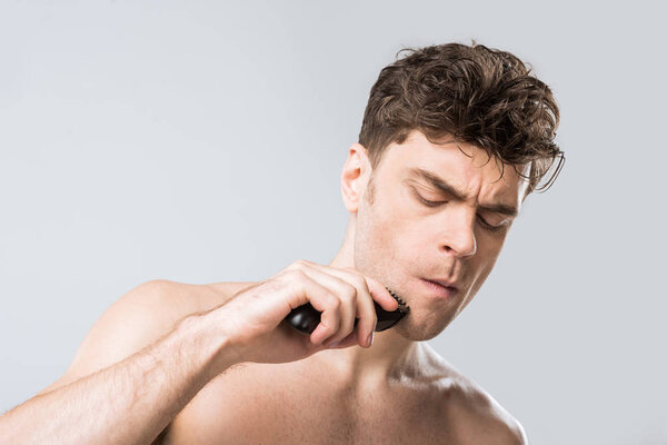 handsome young man shaving with electric razor isolated on grey