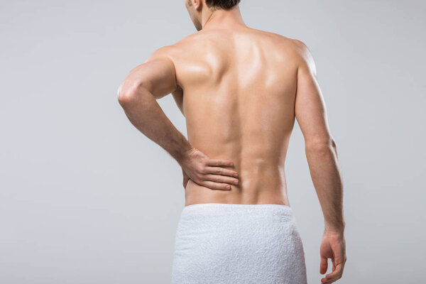 rear view of young man suffering from back pain, isolated on grey