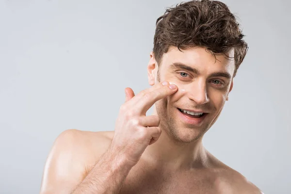 Uomo Sorridente Che Applica Crema Cosmetica Sul Viso Isolata Grigio — Foto Stock