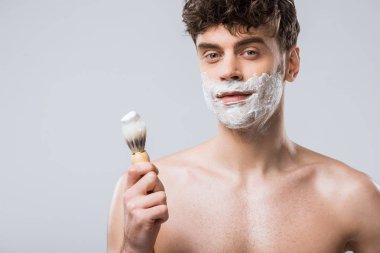 handsome man holding brush with shaving foam, isolated on grey clipart