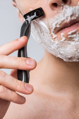 cropped view of young man foam on face shaving with razor, isolated on grey clipart