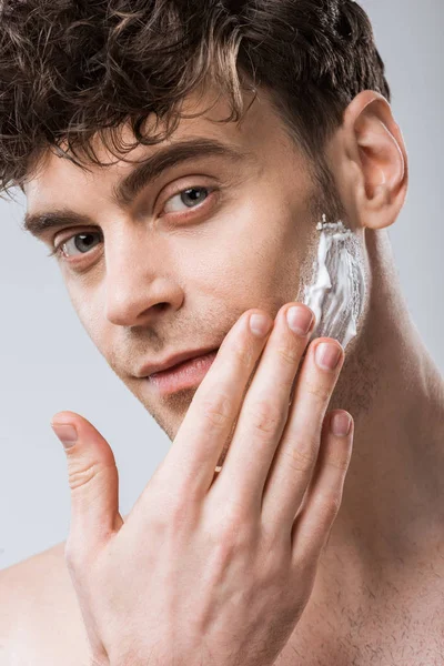 英俊的大男子主义应用剃须泡沫在脸上 隔离在灰色 — 图库照片