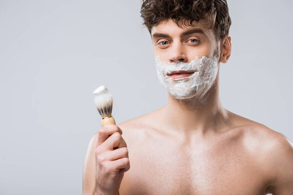 handsome man holding brush with shaving foam, isolated on grey