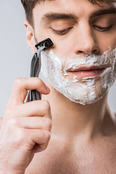 close up of man foam on face shaving with razor, isolated on grey