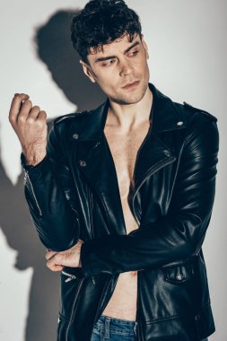 handsome young man posing in black leather jacket on grey
