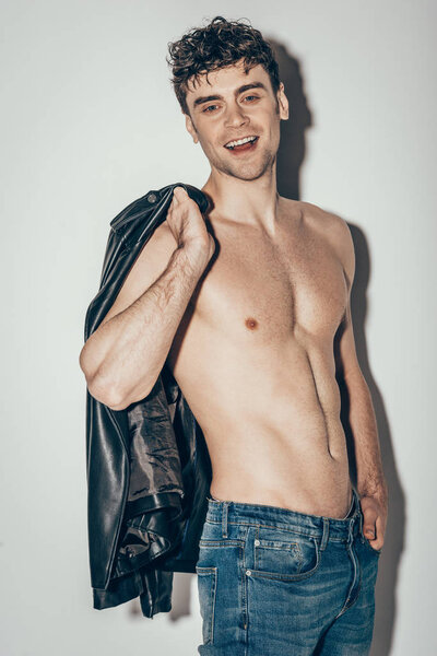 happy shirtless man posing with black leather jacket on grey