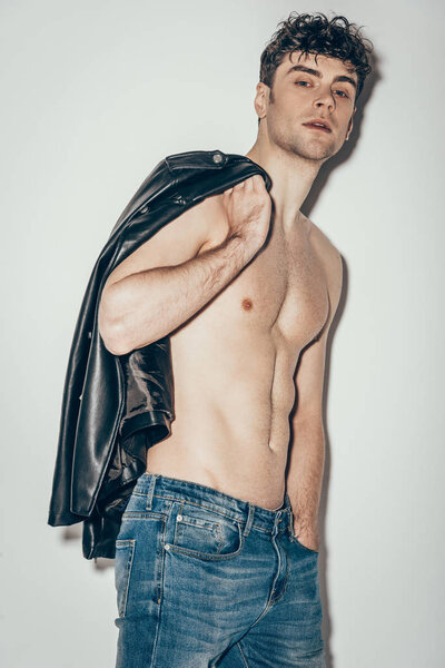 sexy shirtless man posing with black leather jacket on grey