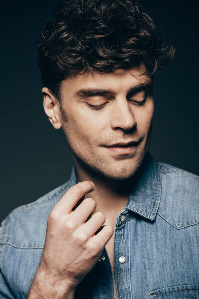 handsome stylish man posing in jeans shirt isolated on dark grey