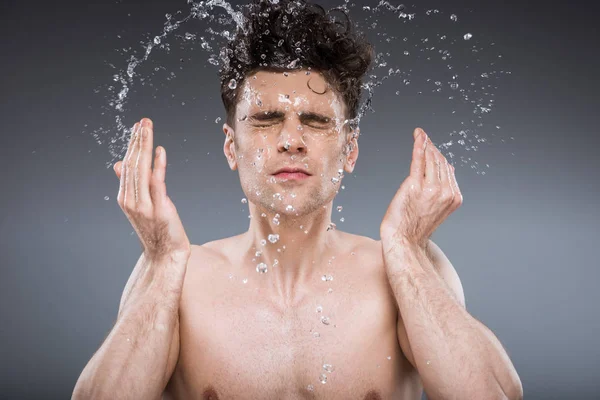 handsome man splashing water into face, isolated on grey