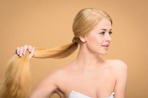 красивая молодая блондинка с длинными волосами и отводя взгляд на бежевый цвет
