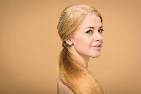 side view of beautiful young blonde woman with long hair smiling at camera isolated on beige