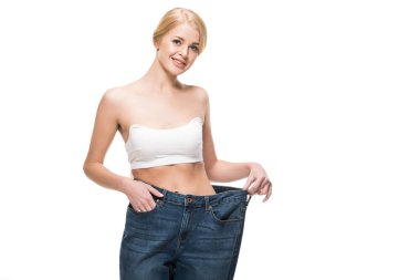 beautiful happy slim woman in oversized jeans smiling at camera isolated on white  