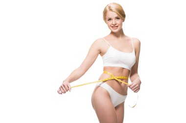 beautiful slim girl in white underwear holding measuring tape around waist and smiling at camera isolated on white clipart