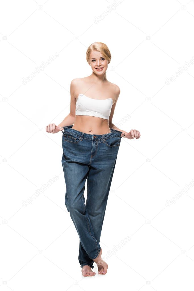 full length view of beautiful happy slim woman in oversized jeans smiling at camera isolated on white  