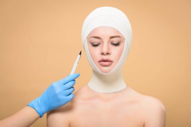 cropped shot of hand in latex glove holding scalpel near woman with bandages over head looking down isolated on beige   clipart