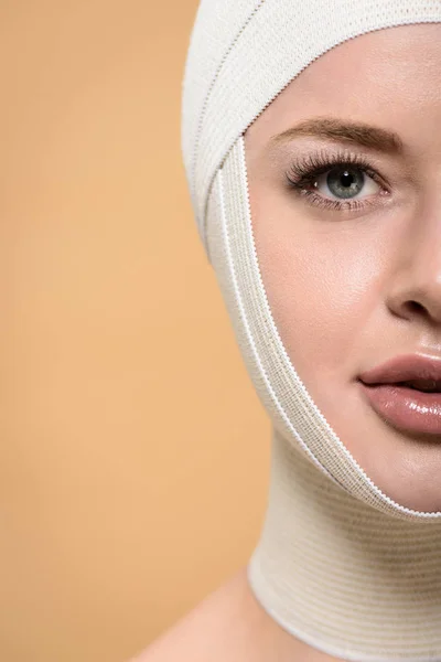half face of young woman with bandages over head looking at camera isolated on beige