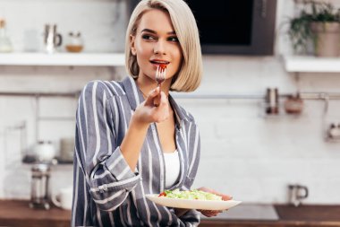 selective focus of attractive woman holding plate and eating salad