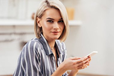 seçici odak olan akıllı telefon tutarak ve kameraya bakarak çekici kadın