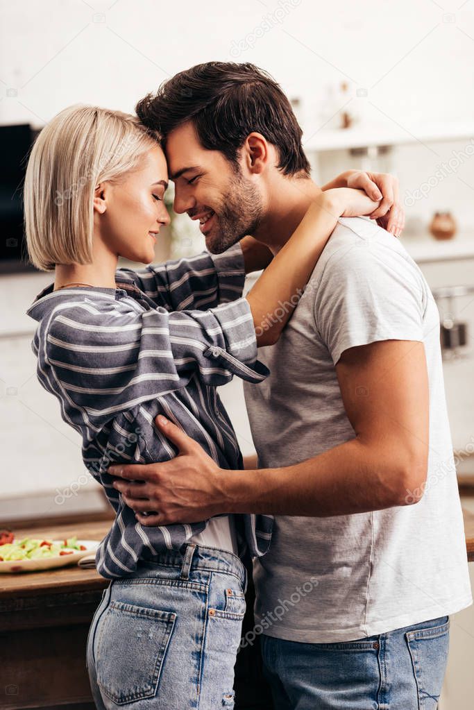 selective focus of handsome boyfriend and attractive girlfriend hugging and smiling in kitchen