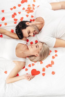 top view of attractive girlfriend and handsome boyfriend smiling and laying near hearts signs on Valentine's day